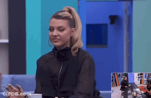 A Woman In A Black Top Is Sitting At A Table With A Cup Of Coffee GIF