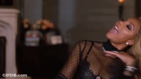 A Woman In A Black Top Is Smiling And Sitting In A Living Room . GIF