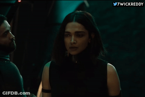A Woman In A Black Top Is Standing Next To A Man In A Dark Room With 7Wickreddy Written On The Bottom GIF