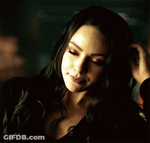 A Woman In A Black Top Is Touching Her Hair GIF