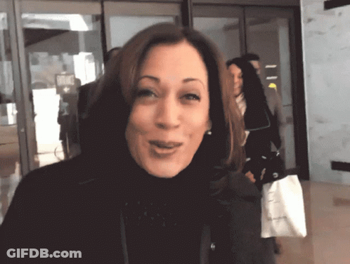 A Woman In A Black Turtleneck Is Smiling And Holding A White Bag That Says ' Calvin Klein ' On It GIF
