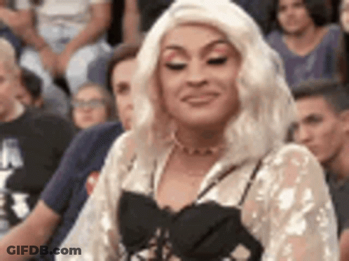 A Woman In A Blonde Wig Is Sitting In A Crowd Of People . GIF