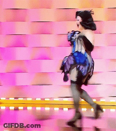 A Woman In A Blue And Black Dress Is Dancing In Front Of A Pink Wall With Janeyjacke Written On The Bottom GIF