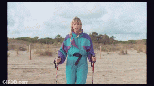 A Woman In A Blue And Purple Ski Suit Holds Walking Poles GIF