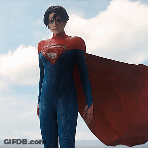A Woman In A Blue And Red Superman Costume Stands In Front Of A Cloudy Sky GIF