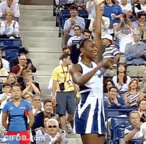 A Woman In A Blue And White Dress Is Raising Her Fist In The Air In Front Of A Crowd GIF