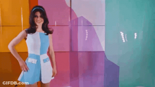 A Woman In A Blue And White Dress Is Standing In Front Of A Colorful Wall With A Hole In It . GIF