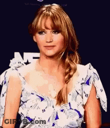 A Woman In A Blue And White Floral Dress Is Sitting In Front Of A Blue Background . GIF