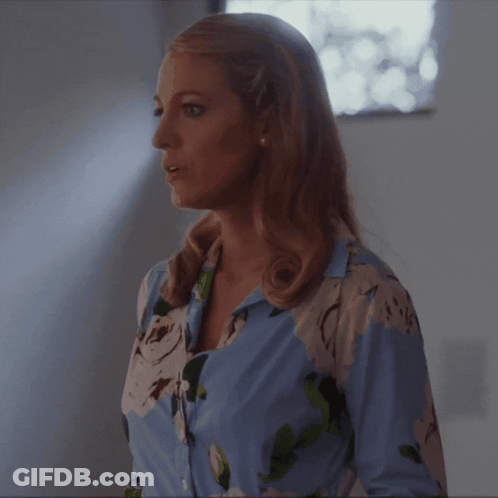 A Woman In A Blue And White Floral Shirt Is Standing In Front Of A Window GIF
