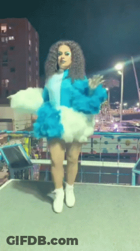 A Woman In A Blue And White Outfit Is Standing On A Stage GIF
