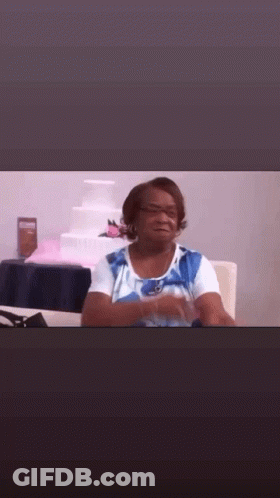 A Woman In A Blue And White Shirt Is Sitting At A Table In Front Of A Wedding Cake . GIF