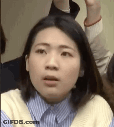 A Woman In A Blue And White Striped Shirt Is Making A Funny Face While Sitting In A Crowd . GIF