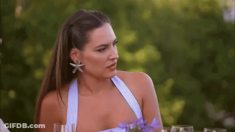 A Woman In A Blue And White Striped Top Is Sitting At A Table With Wine Glasses . GIF