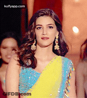 A Woman In A Blue And Yellow Saree Is Standing In Front Of A Group Of Women . GIF