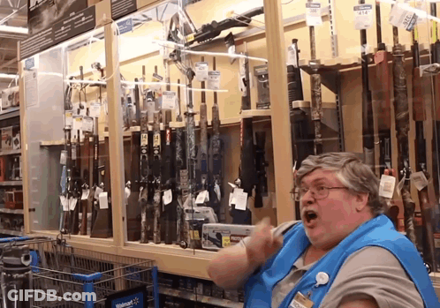 A Woman In A Blue Apron Is Standing In Front Of A Walmart Display Of Guns GIF