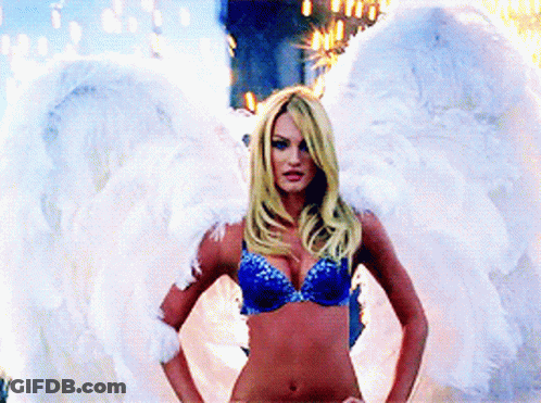 A Woman In A Blue Bra And White Angel Wings Stands With Her Hands On Her Hips GIF