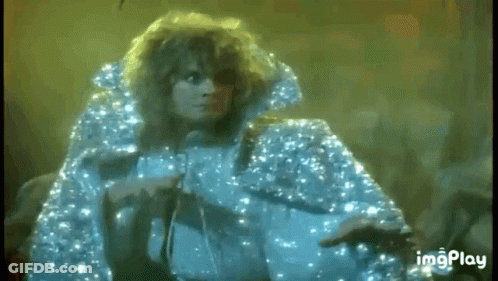 A Woman In A Blue Cape Is Singing Into A Microphone On Stage . GIF