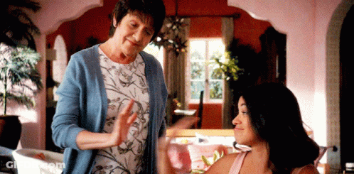 A Woman In A Blue Cardigan Is Standing Next To A Woman In A Pink Tank Top . GIF