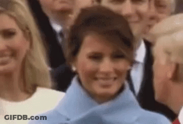 A Woman In A Blue Coat Is Smiling In Front Of A Crowd . GIF