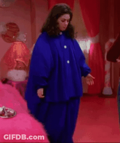 A Woman In A Blue Coat Is Standing In A Bedroom GIF