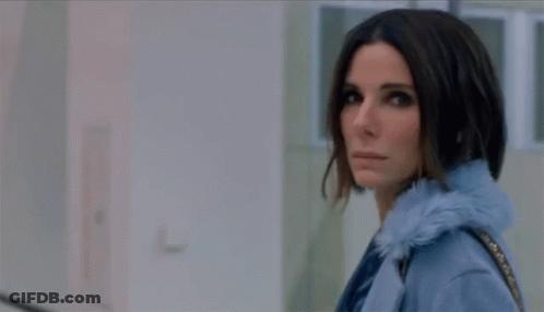 A Woman In A Blue Coat Is Standing In A Hallway Looking At The Camera GIF