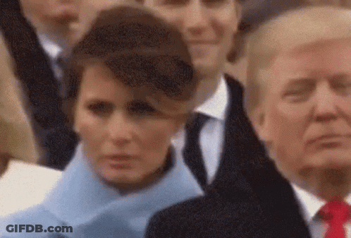 A Woman In A Blue Coat Is Standing Next To A Man In A Suit And Tie Giving A Thumbs Up . GIF
