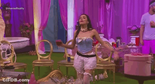 A Woman In A Blue Corset Is Dancing In A Room With Purple Curtains And Gold Chairs . GIF
