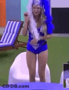 A Woman In A Blue Costume Is Standing In Front Of A Table Holding A Feather Boa . GIF