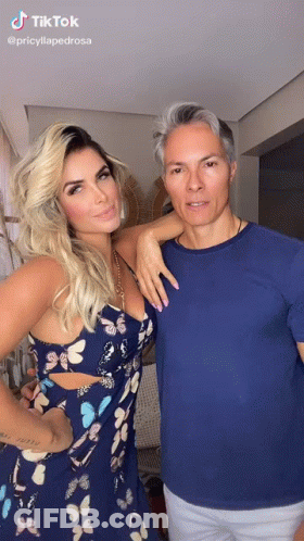 A Woman In A Blue Dress And A Man In A Blue Shirt Are Standing Next To Each Other . GIF