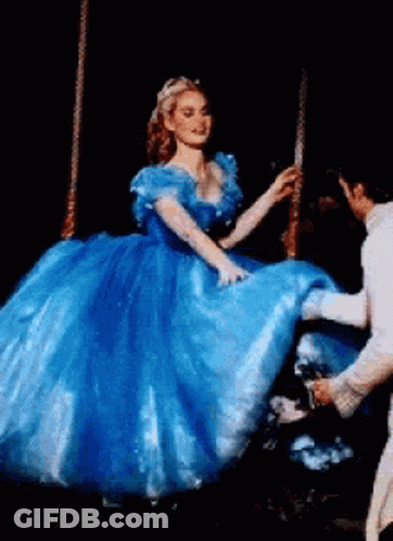 A Woman In A Blue Dress Is Being Helped Up By A Man In A White Suit . GIF