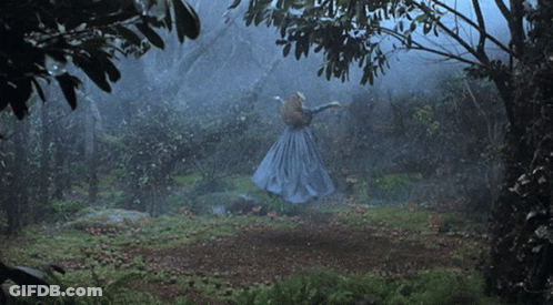 A Woman In A Blue Dress Is Dancing In A Dark Forest GIF