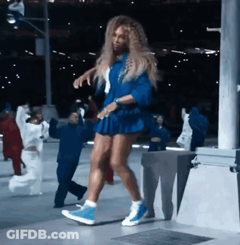 A Woman In A Blue Dress Is Dancing In Front Of A Group Of People GIF