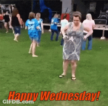 A Woman In A Blue Dress Is Dancing In The Grass With The Words Happy Wednesday Written Above Her GIF