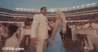 A Woman In A Blue Dress Is Dancing With A Man In A White Suit In A Stadium With The Words Music On The Bottom GIF