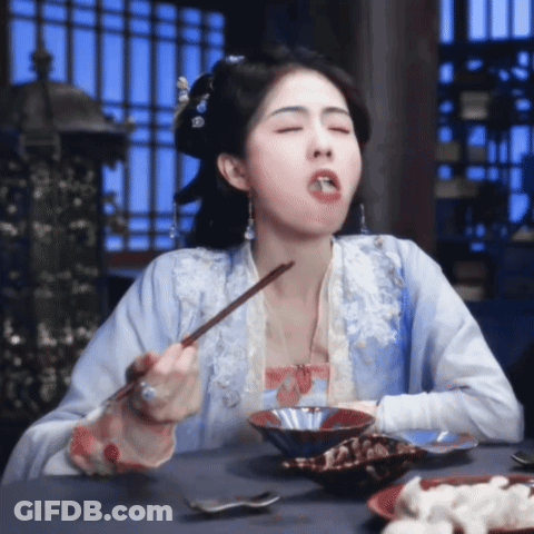 A Woman In A Blue Dress Is Eating Food With Chopsticks GIF