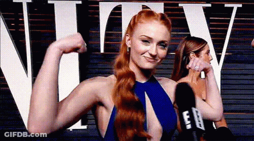 A Woman In A Blue Dress Is Flexing Her Muscles In Front Of A Microphone . GIF