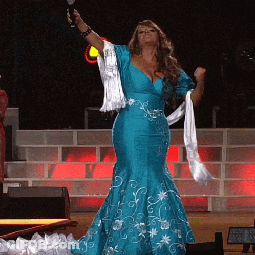 A Woman In A Blue Dress Is Holding A Microphone In Her Hand GIF