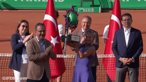 A Woman In A Blue Dress Is Holding A Trophy In Front Of A Sign That Says Teb GIF