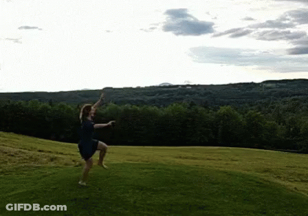 A Woman In A Blue Dress Is Jumping In The Air In A Grassy Field GIF