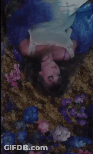 A Woman In A Blue Dress Is Laying In A Bed Of Flowers . GIF