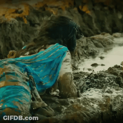 A Woman In A Blue Dress Is Laying In The Mud On The Beach GIF