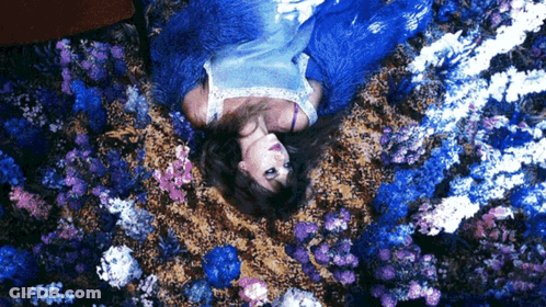 A Woman In A Blue Dress Is Laying On Her Back In A Field Of Blue Flowers GIF