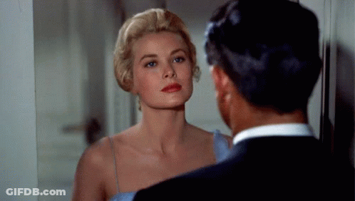 A Woman In A Blue Dress Is Looking At Herself In A Mirror While A Man In A Suit Looks On . GIF