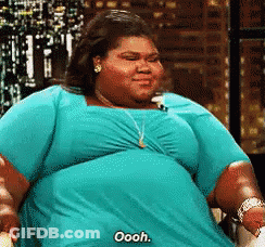 A Woman In A Blue Dress Is Saying Oooh While Sitting In A Chair . GIF