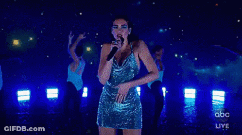 A Woman In A Blue Dress Is Singing Into A Microphone On Stage . GIF