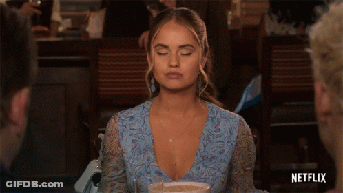 A Woman In A Blue Dress Is Sitting At A Table With A Netflix Logo In The Corner GIF
