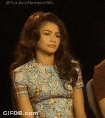 A Woman In A Blue Dress Is Sitting In A Chair And Looking At The Camera . GIF