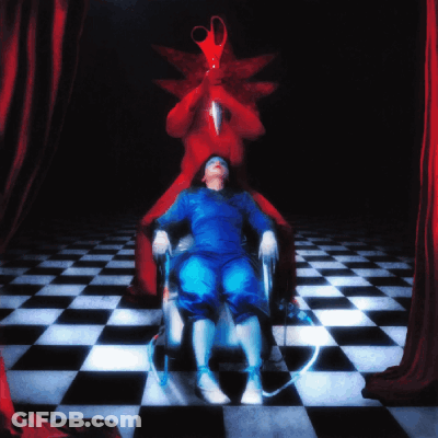 A Woman In A Blue Dress Is Sitting In A Chair In Front Of A Red Curtain With A Pair Of Scissors On Her Head GIF