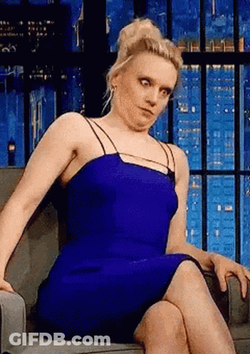 A Woman In A Blue Dress Is Sitting In A Chair Making A Funny Face GIF
