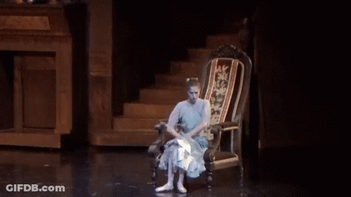 A Woman In A Blue Dress Is Sitting In A Chair On A Stage GIF